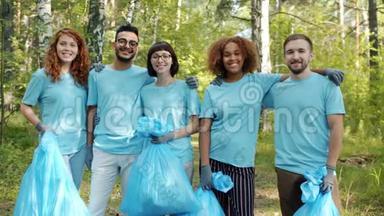 快乐的<strong>青年志愿者</strong>带着垃圾袋站在森林里拥抱微笑